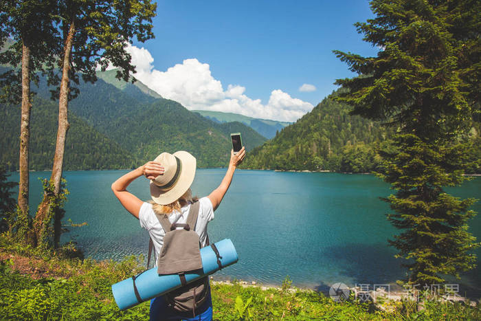 照片 美丽的女孩旅行者使自拍在一个大的蓝色山湖在山的背景旅行概念