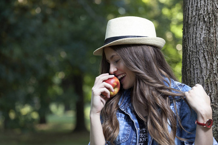拿着帽子享受大自然和吃苹果的年轻女子