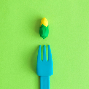平放置塑料叉子和小橡胶玉米玩具对绿色背景最小创造性的素食概念