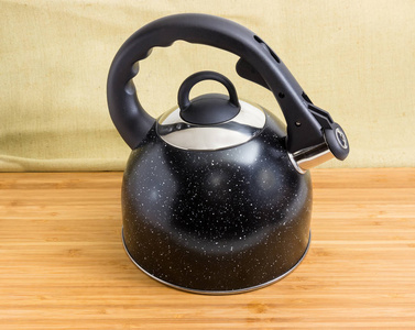现代黑色不锈钢炉顶壶盖, 黑色塑料手柄和蒸汽哨子内置在一个竹木表面的壶嘴
