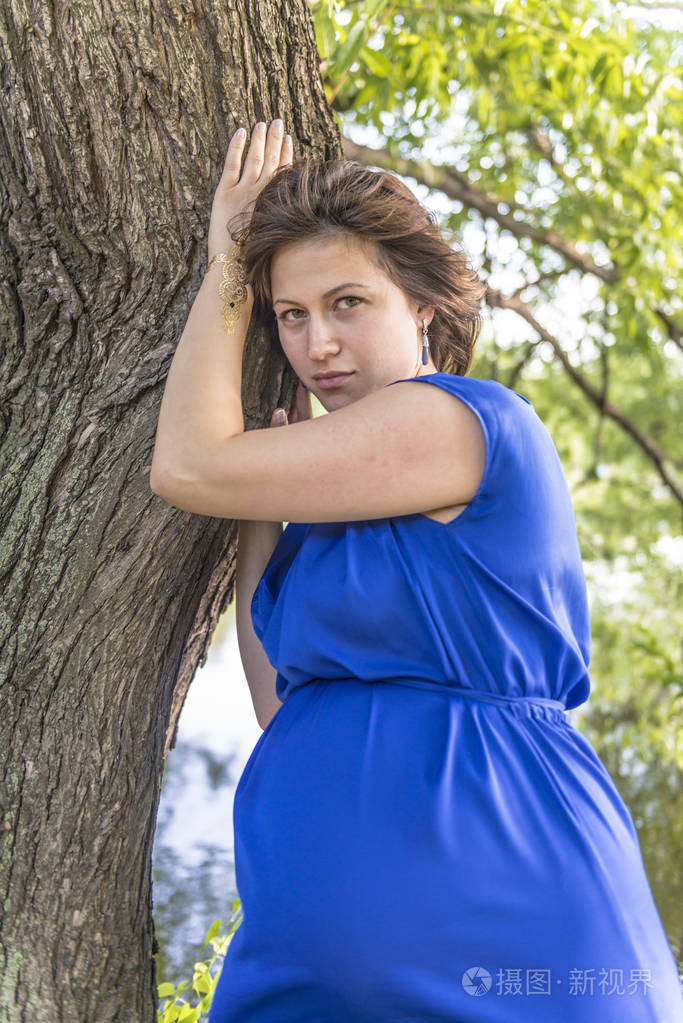 穿着蓝色连衣裙的孕妇在公园里散步