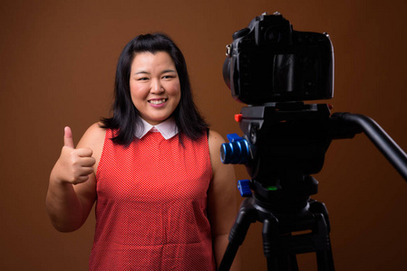 超重亚洲妇女视频博客在工作室与数码单反相机上三脚架