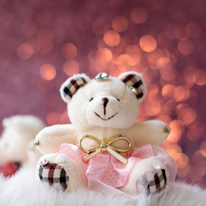小泰迪熊娃娃的特写图像坐在白色的地毯与模糊粉红色的颜色散景背景