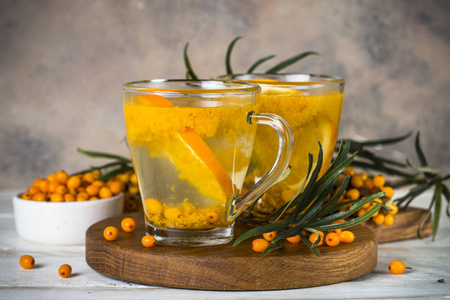 沙棘茶与橙色在玻璃杯与新鲜沙棘浆果和叶子。草药维他命茶