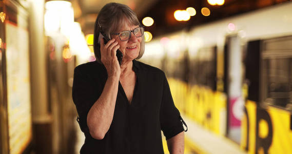 在等待火车的同时, 用手机与家人聊天的愉快的老太太