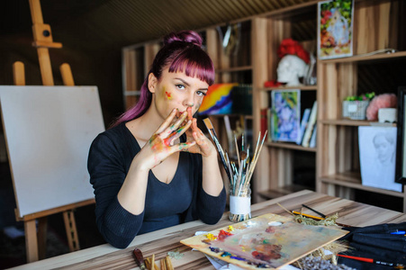 关闭美丽的女性艺术家的肖像与紫色的头发和肮脏的手, 在他们不同的油漆, 考虑她的新项目
