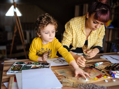 年轻的母亲和她的儿子在艺术工作室里玩彩色颜料, 并在他们身上涂上颜色肮脏的手。