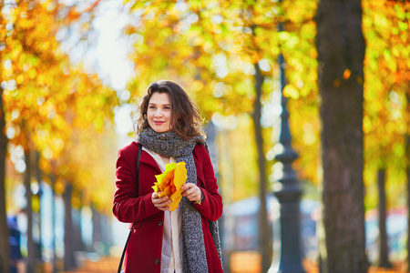 在一个阳光明媚的秋日金色树叶秋天公园美丽的少女，控股黄色的叶子在她的手