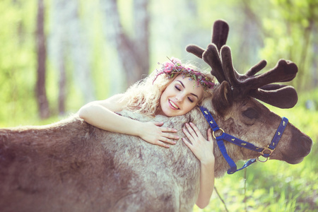 鹿茸粉漂亮的女孩在森林中拥抱一只驯鹿照片