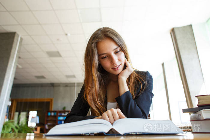 照片 一个微笑的女学生, 在图书馆的书桌上看书.