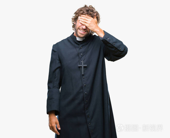 英俊的西班牙天主教教士人在孤立的背景微笑和笑用手在脸上覆盖眼睛为
