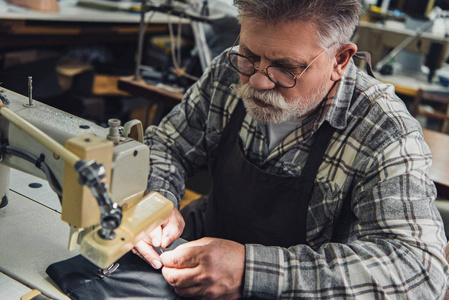 在演播室缝纫机上工作的男性手袋工匠的高视角
