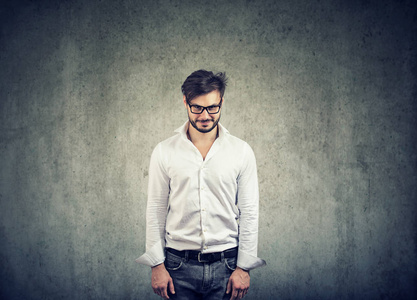 成人胡子男子在眼镜看狡猾的相机站立害羞地在灰色背景照片
