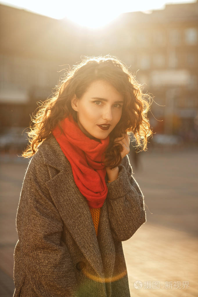 城市肖像的优雅黑发妇女与波浪头发穿大衣, 摆在阳光眩光在街上