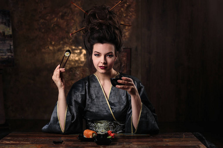 穿着艺妓亚洲服装的感性年轻女子, 穿着时尚化妆和发型的服装, 喝着茶, 吃寿司, 时装美像
