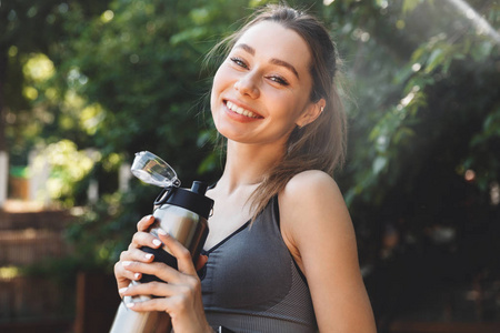 一个满意的年轻健身女孩的肖像手持水壶户外