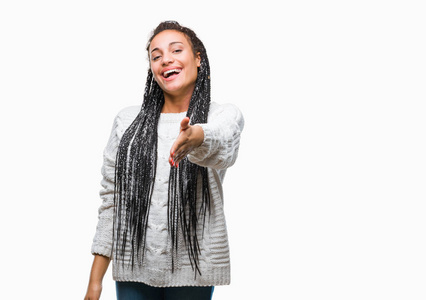 年轻的编织头发非洲裔美国女孩穿着毛衣在孤立的背景微笑友好提供握手作为问候和欢迎。成功的业务