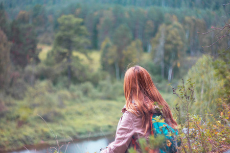 女孩旅行者以红色长的头发坐和看狂放的自然