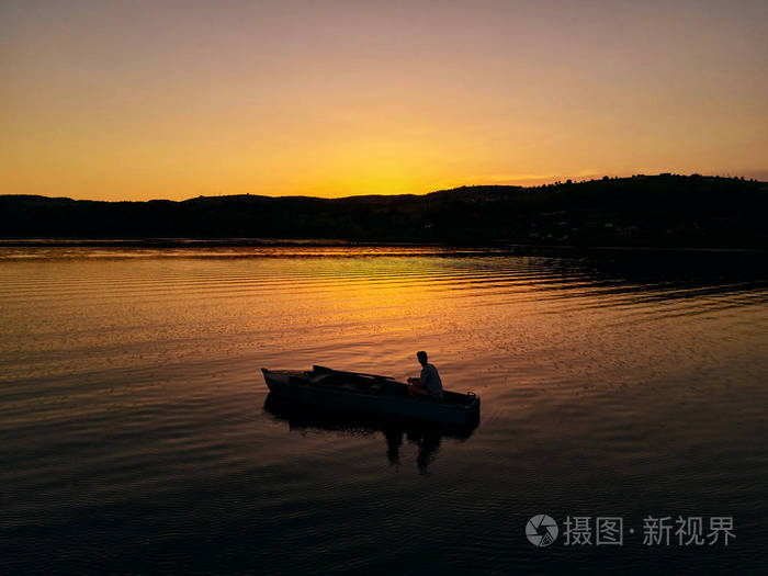孤独的家伙坐在小船在日落