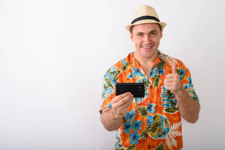 工作室拍摄年轻快乐肌肉发达的游客男子微笑, 而与手机拍照, 并在白色背景下竖起大拇指
