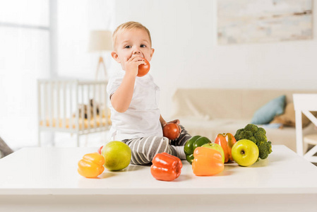 可爱的幼儿吃饭和坐在桌子上周围的水果和蔬菜