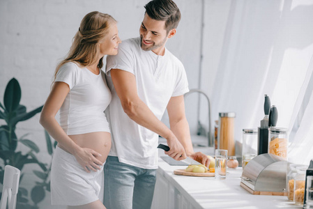 微笑的人画像在柜台与怀孕的妻子在家庭厨房附近切开果子