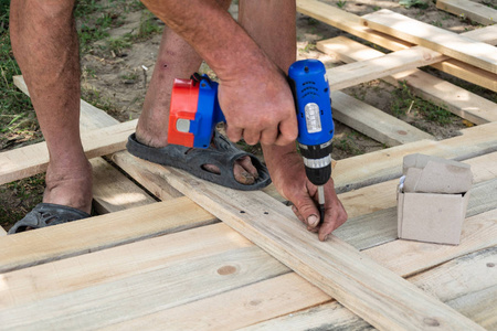 钻木车间。木工和人概念木匠用电池力量钻钻木板在车间, 模板为篱芭