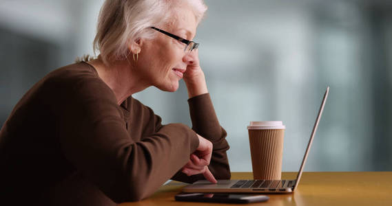 现代女性老人在办公楼内浏览互联网和喝咖啡