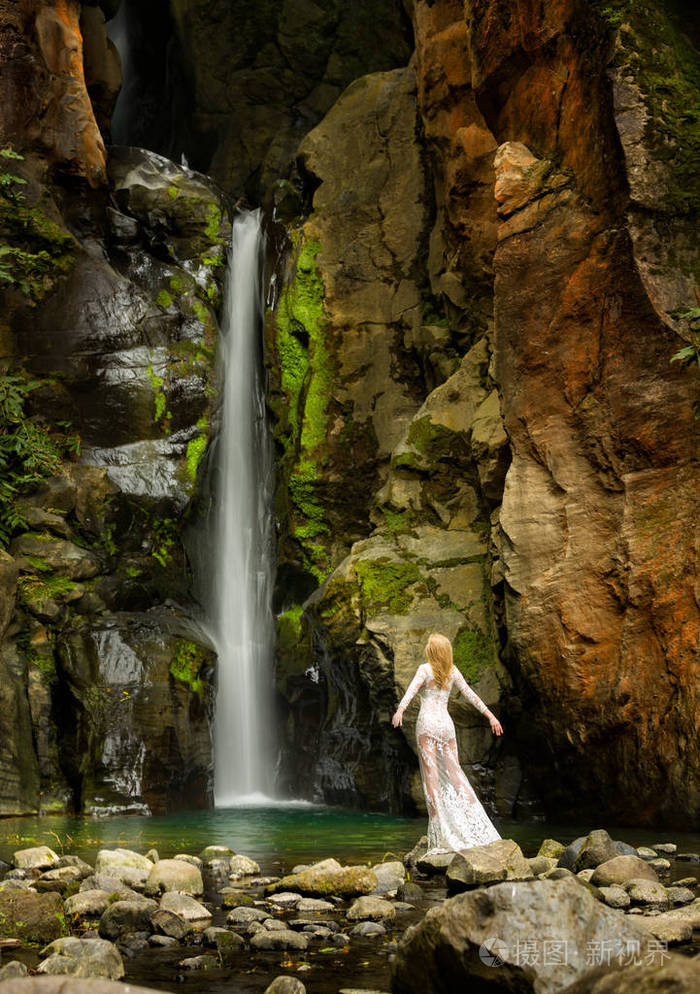 美丽的长发金发女郎在白色花边礼服站立下的瀑布在亚速尔群岛群岛