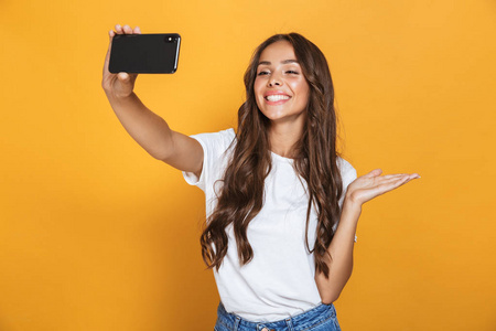 正面女人的肖像20s 与长发笑, 而拍摄自拍照片上的智能手机查出的黄色背景