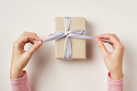 妇女的手解开弓在礼品盒上白色背景, 顶部视图