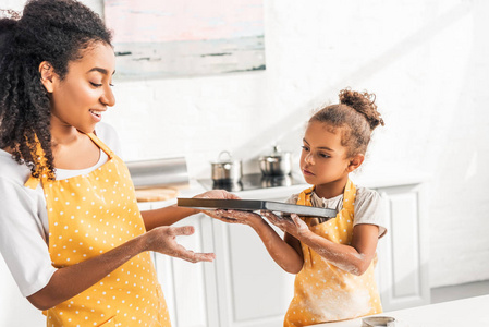 非洲裔美国母女和女儿拿着托盘与未烘焙饼干在厨房