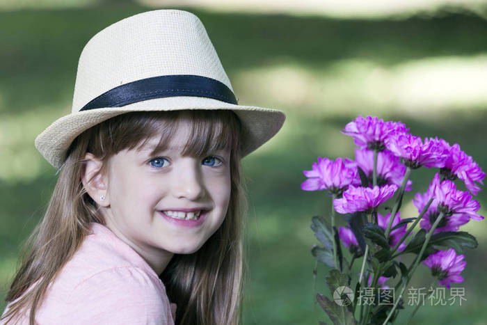 小可爱的微笑的女孩, 帽子看着相机, 拿着一束鲜花