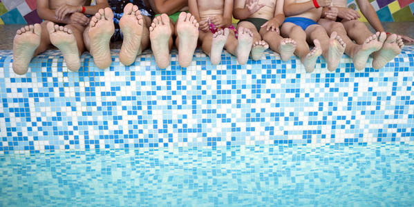 一群人腿坐在游泳池边上。一群朋友或父母与孩子在游泳池边上的脚