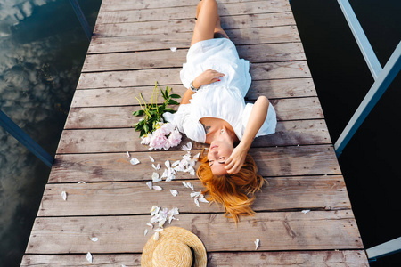 有魅力的年轻时髦女人穿着白色连衣裙躺在木地板上