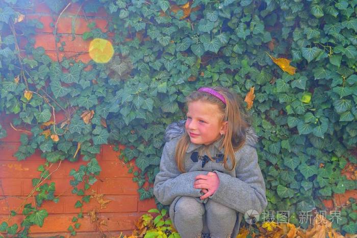 秋天, 小女孩穿着复古外套, 蹲在砖墙前.秋天的常春藤墙.秋天的概念.