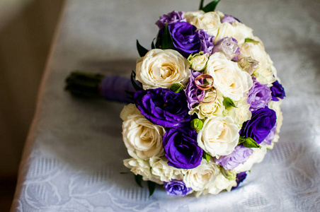 紫罗兰和白色的花朵花束与金色的戒指在桌子上