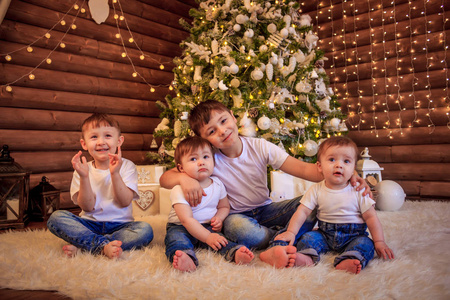 孩子们坐在圣诞树下。兄弟姐妹们坐在树下等待礼物。新年和圣诞节