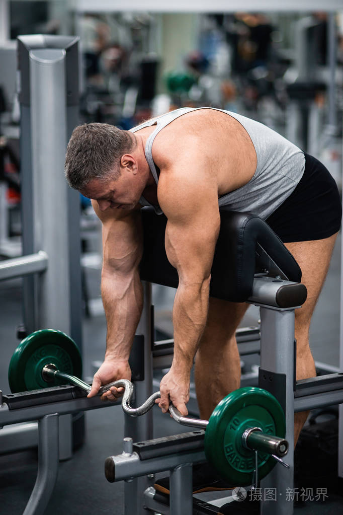 大型运动员在健身房训练.用板凳上的杠铃训练二头肌