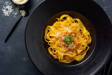 费图西辛意大利面食与传统的意大利帕萨酱和帕尔马奶酪在黑色的盘子在黑暗的背景。顶视图