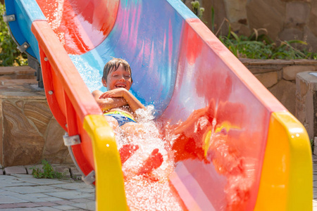 一个快乐的男孩在水中滑在一个游泳池在一个美丽的水上公园的暑假乐趣。一个男孩滑行在水中滑动和飞溅