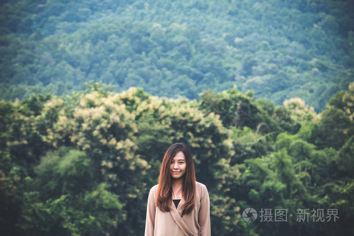 一个美丽的亚洲女人, 带着笑脸独自站在绿色自然和山地背景上