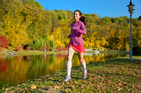 在秋天公园，美丽的女孩跑慢跑在户外跑步的女人