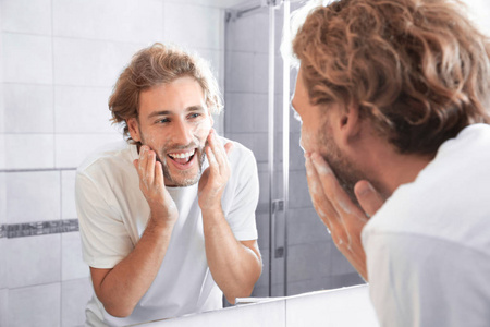 在浴室用镜子附近用肥皂洗脸的年轻人