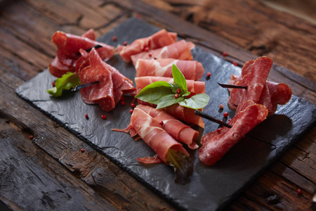 黑色背景的意大利火腿 crudo 或 jamon 与新鲜罗勒叶子的切片