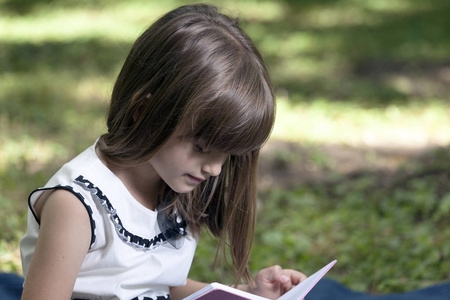 阅读一本书时自然中可爱的小女孩的肖像