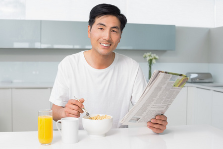 在厨房里看着报纸同时有谷物的男人微笑着