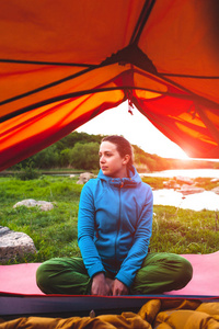 女孩坐在帐篷附近。一个在睡袋里的女人。一个微笑的黑发人在自然休息。在河边露营