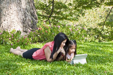 小的亚洲女孩和妈妈喜欢在公园里的平板电脑