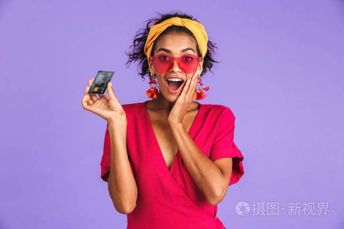 一个兴奋的年轻非洲妇女的肖像站在紫罗兰色背景, 显示塑料信用卡